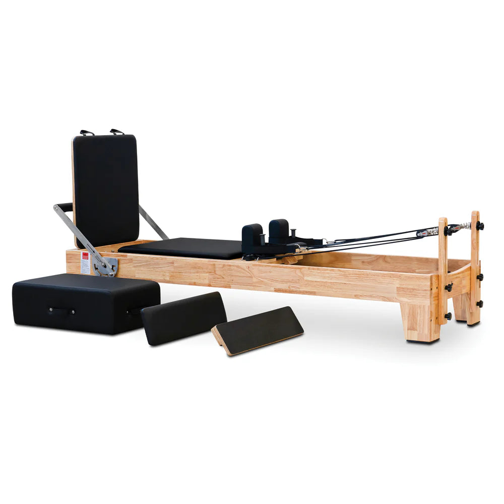 Angled front view of the Impact Fitness Pilates Reformer in Oakwood with black carriage, showing jumpboard attachment and extra accessories.