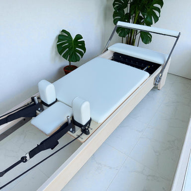 Angled aerial view of Carriage for Milaron Maple Studio Reformer with creme carriage and frame.  Footbar is up