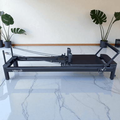 Full side view of pilates reformer machine in home setting with black frame and black carriage