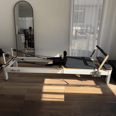 Full side view of Milaron pearl pilates machine in the home with white frame and black carriage