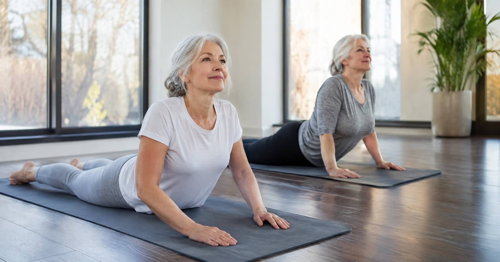 Two senior woman doing cobra pose on yoga mats in studio