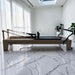 Milaron Maple Studio V3 Pilates reformer with a solid maple frame and black microfibre leather upholstery, set up in a sunlit room