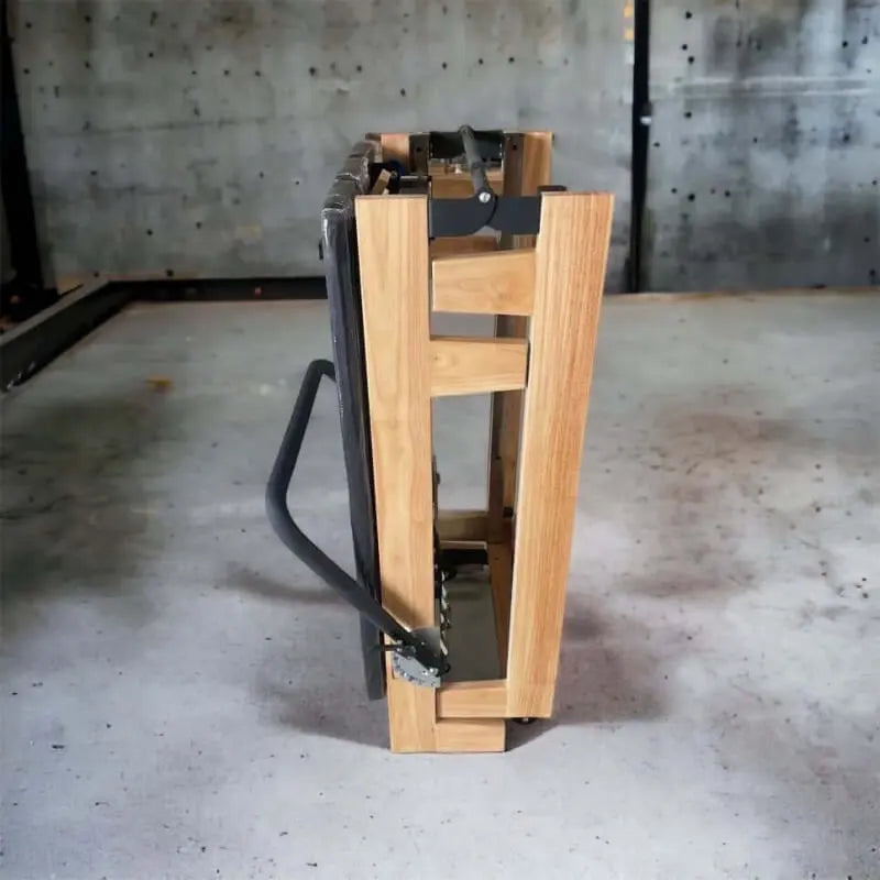 Wooden foldable reformer bed in folded position side on view in concrete room