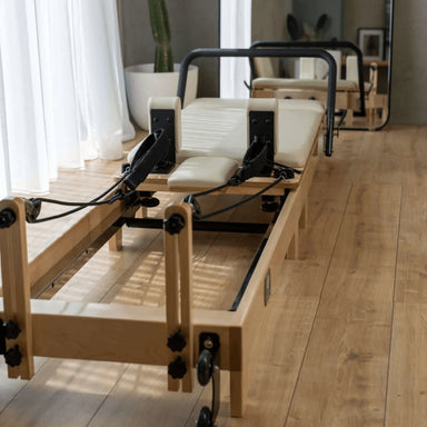 Core Collab Wooden Pilates reformer machine in beige in a studio or home setting with wooden flooring and large windows.