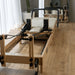 Core Collab Wooden Pilates reformer machine in beige in a studio or home setting with wooden flooring and large windows.