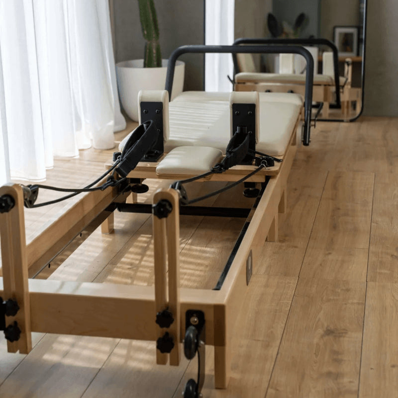 Core Collab Wooden Pilates reformer machine in beige in a studio or home setting with wooden flooring and large windows.