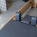 Close up aerial view of carriage and head and shoulder rest of a wooden pilates reformer machine with grey upholstery