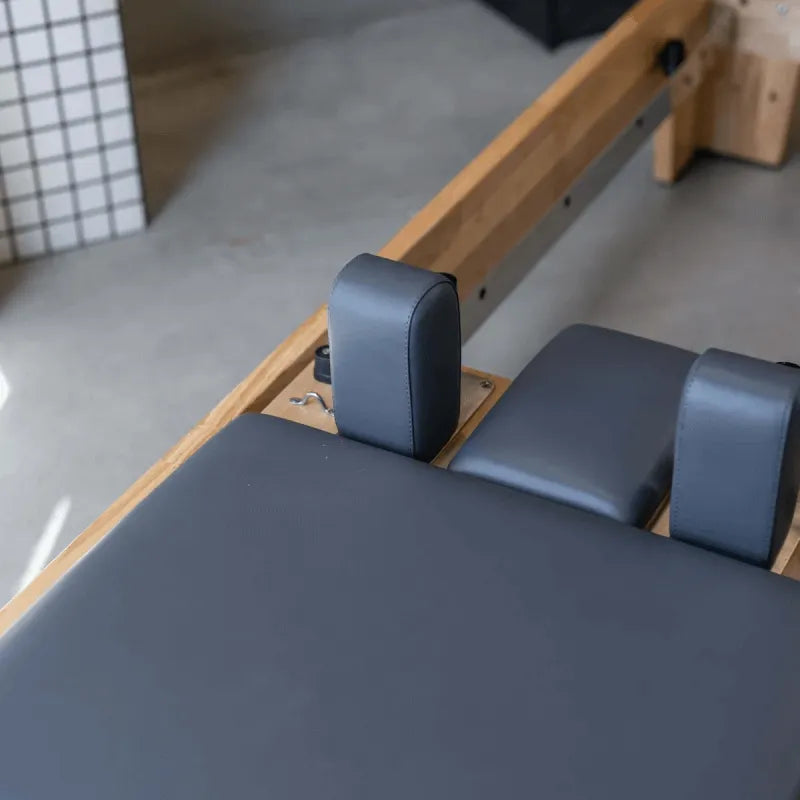 Close up aerial view of carriage and head and shoulder rest of a wooden pilates reformer machine with grey upholstery