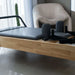 Close up side view of pilates reformer bed carriage with wooden frame and grey upholstery in home setting 