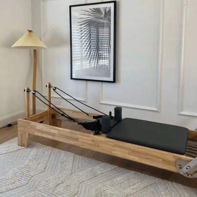 Wooden pilates reformer bed with black upholstery in home living room setting