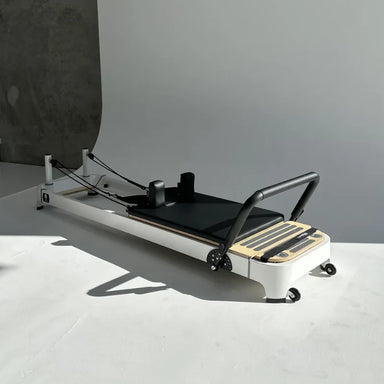 Core Collab Queen 2.0 Pilates reformer machine with white frame and black carriage on a light gray photo shoot background