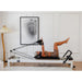 Lady using Core Collab Queen Studio Reformer with white frame and black upholstery in home living room