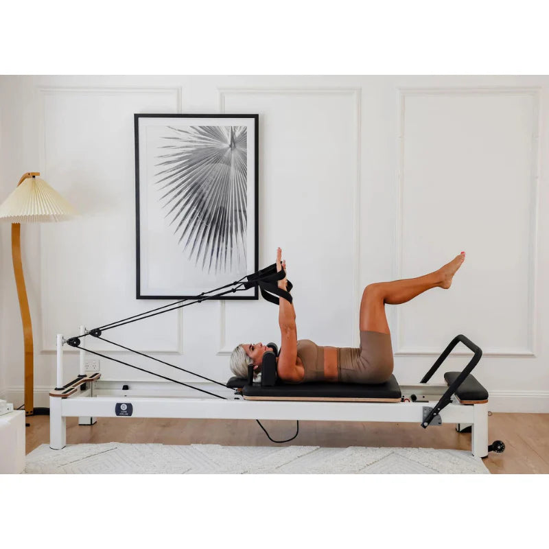 Lady using Core Collab Queen Studio Reformer with white frame and black upholstery in home living room