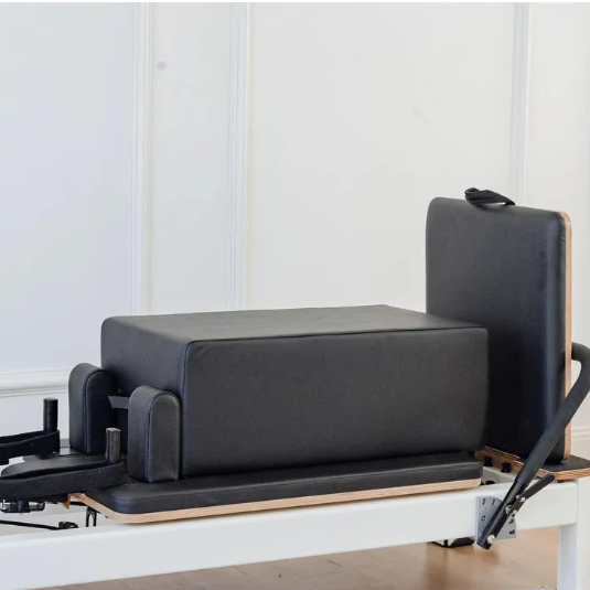 Close up of pilates reformer with sitting box and jumpboard attached with black upholstery 