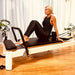 Woman exercising on Core Collab Pilates reformer machine in a home setting.