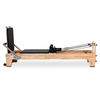 Side view of the Impact Fitness Pilates Reformer in Oakwood with black carriage, showing jumpboard attachment.