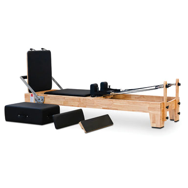 Angled front view of the Impact Fitness Pilates Reformer in Oakwood with black carriage, showing jumpboard attachment and extra accessories.