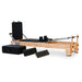 Angled front view of the Impact Fitness Pilates Reformer in Oakwood with black carriage, showing jumpboard attachment and extra accessories.