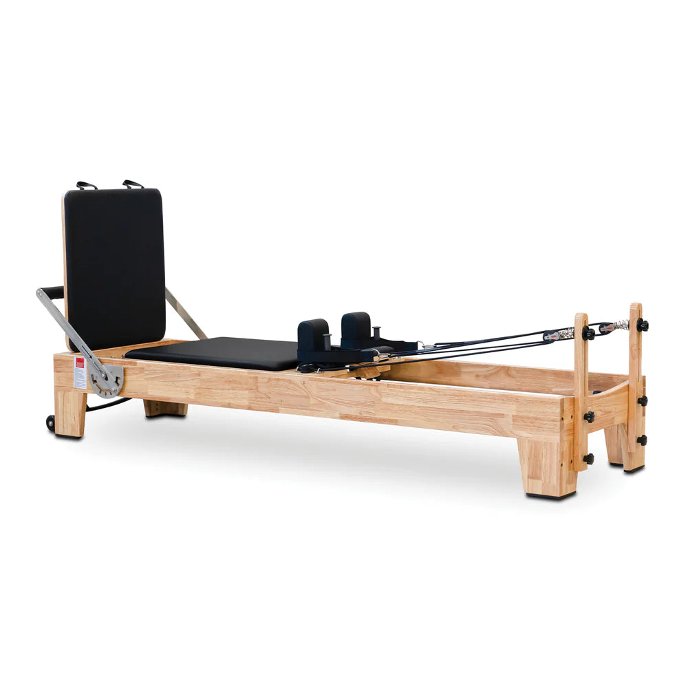 Angled front view of the Impact Fitness Pilates Reformer in Oakwood with black carriage, showing jumpboard attachment 