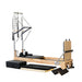 Angled Front View of Impact Fitness Pilates Reformer Machine in Oakwood with Half Trapeze showing Trapeze Springs and bars and extra accessories