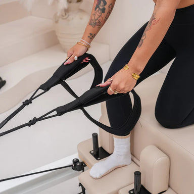 Person kneeling on pilates reformer and pulling on arm straps
