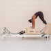 Girl doing downward dog on beige and white pilates reformer on white background