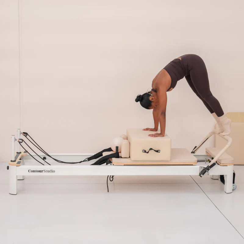 Girl doing downward dog on beige and white pilates reformer on white background