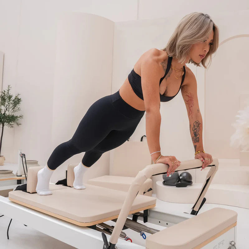Woman in push up position holding footbard of beige and white reformer