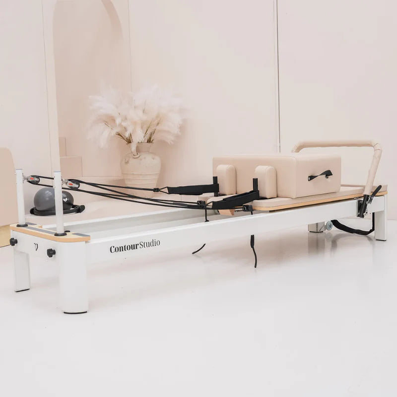 Side view of white pilates reformer with beige leather in a minimal studio