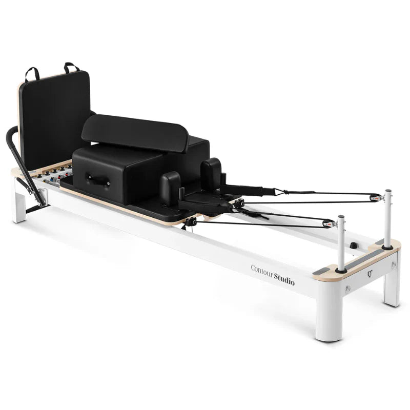 Slight aerial view of pilates reformer with white frame and black upholstery on white background with accessories attached