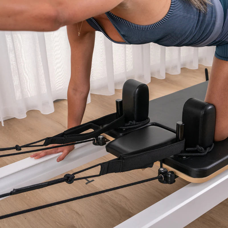 Close up of woman kneeling on carriage of black reformer bed