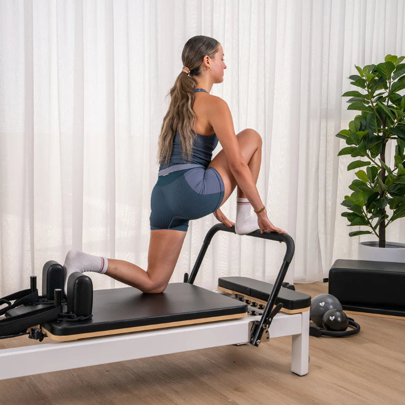 Woman with foot on footbar of black and white pilates reformer machine 