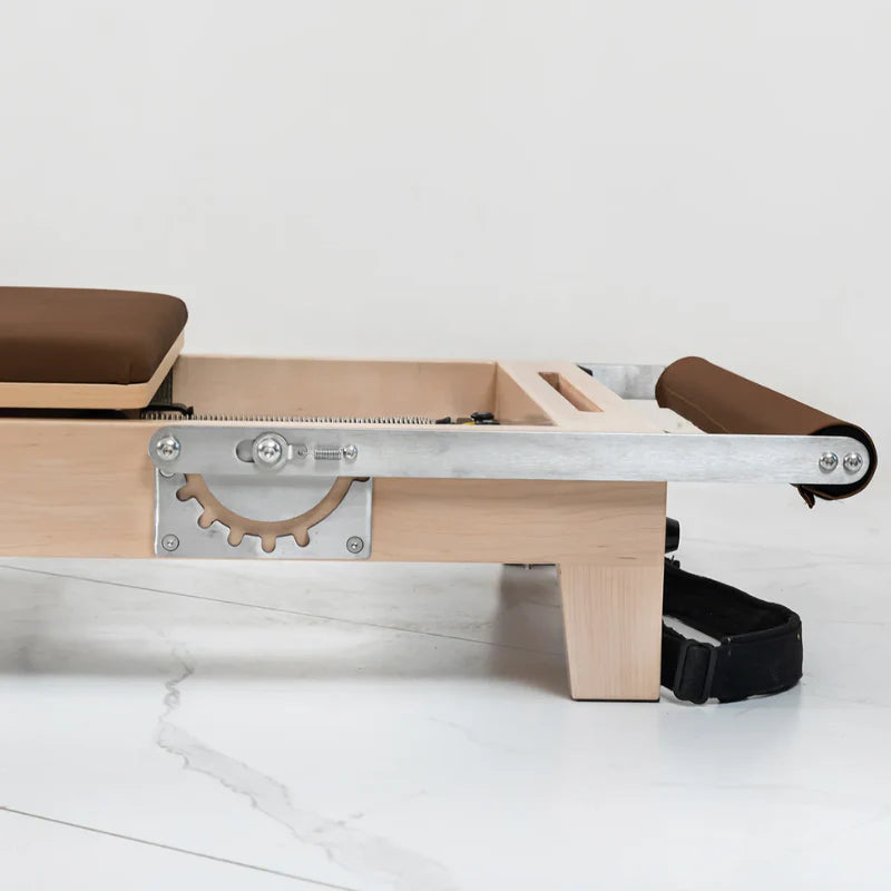 Close up wooden pilates reformer machine with footbar lowered on white background