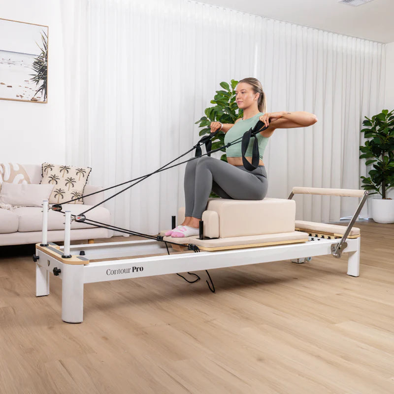 Woman exercising on White Aluminium Contour Pilates reformer machine in a home setting.