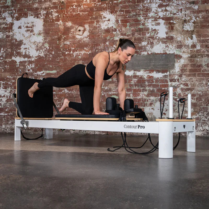 Woman exercising on a  White Aluminium Pilates reformer machine against a brick wall.