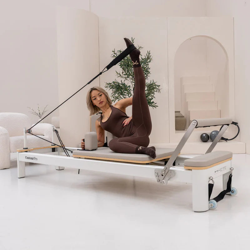 Woman exercising on a Pilates reformer machine in a modern studio.