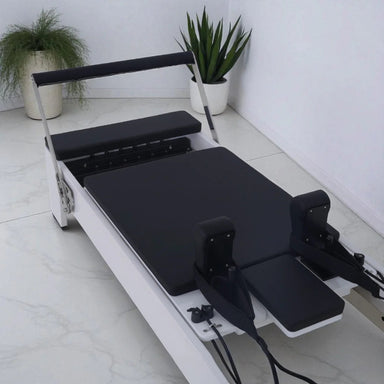 Milaron Blanc Reformer Close Up of Black Carriage with White Frame footbar up on tiiled floor with plants in background
