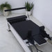 Milaron Blanc Reformer Close Up of Black Carriage with White Frame footbar up on tiiled floor with plants in background
