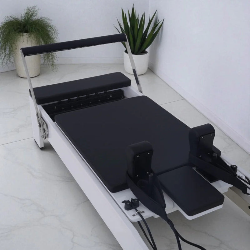 Milaron Blanc Reformer Close Up of Black Carriage with White Frame footbar up on tiiled floor with plants in background
