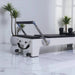 Milaron Blanc White Pilates reformer with black upholstery in a room with plants white marble floors.