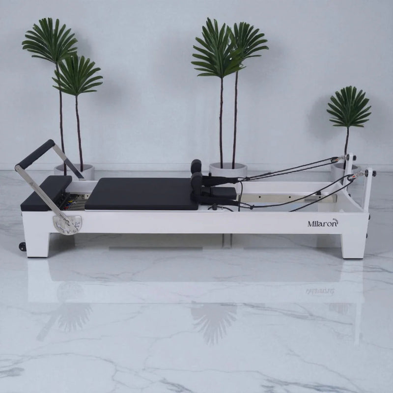 Milaron Blanc Pilates reformer machine showing full side view with white frame and black carriage in white room with plants in background