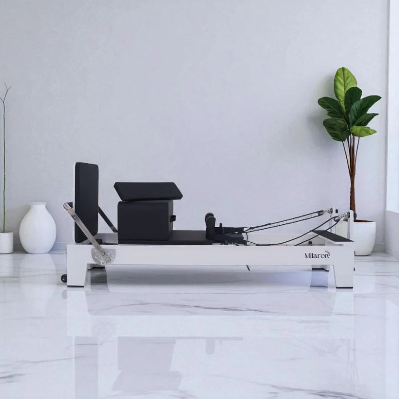 Milaron Blanc Pilates reformer machine with white frame and black carriage in white room with plant and accessories on carriage