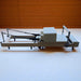 Full side view of Milaron Maple Foldable reformer in studio setting with straps hooked on to hooks near headrest. Also shows sitting box sitting on the carriage