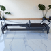 Full side view of pilates reformer machine in home setting with black frame and black carriage
