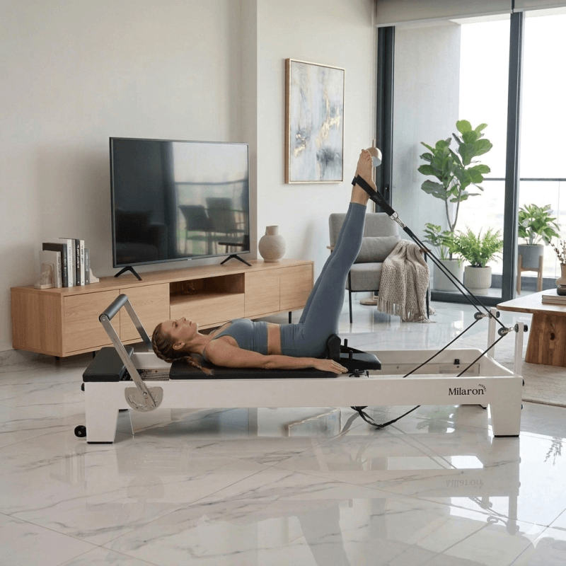 Woman using a Milaron Blanc V2 Pilates reformer machine in a modern living room.