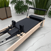 Milaron Pilates reformer machine with maple wood frame and black upholstery on a marble floor with plants in the background