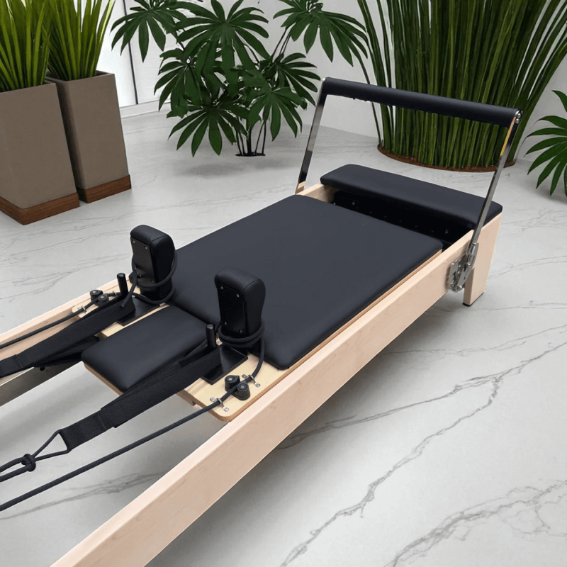 Milaron Pilates reformer machine with maple wood frame and black upholstery on a marble floor with plants in the background