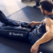 Man using Black Therabody RecoveryAir Jetboots PRIME on his leg in a gym setting