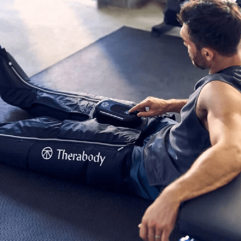 Man using Black Therabody RecoveryAir Jetboots PRIME on his leg in a gym setting