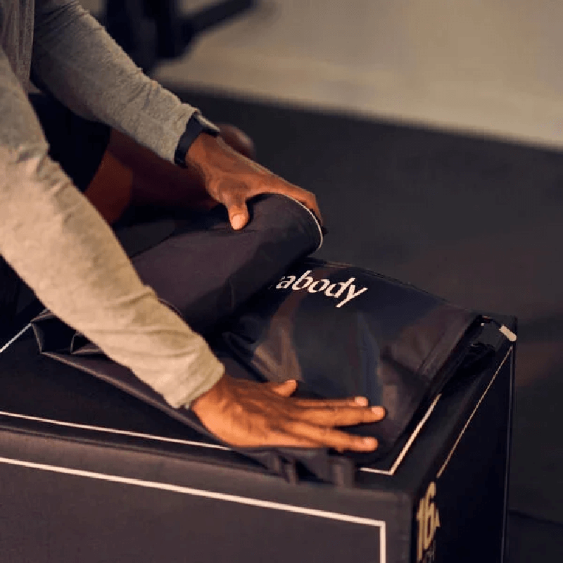 Person rolling Black Therabody RecoveryAir Jetboots PRIME on a black box for storage 